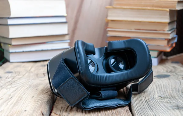 Books VS Virtual Reality: VR-headsets on table, old paper books on background