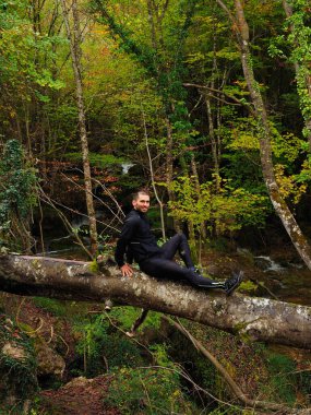 Genç adam ormandaki bir ağaç gövdesine oturur.