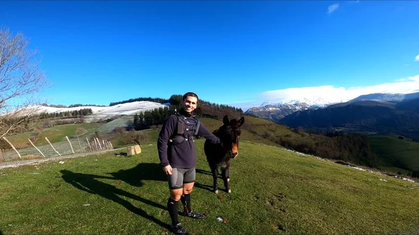 Genç adam bir eşekle dağlarda koşuyor.