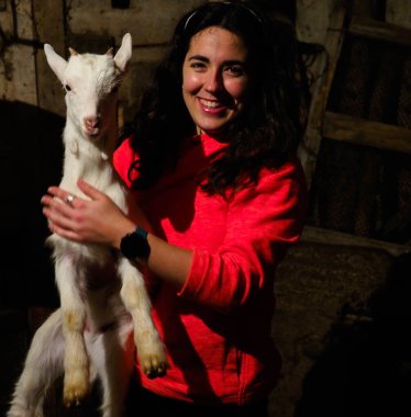 Genç bir kadın beyaz bir keçi tutuyor.