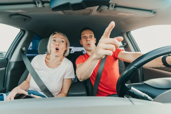 Homem e mulher surpreendidos apontam os dedos para um acidente incrível enquanto conduzem o carro. Pessoas chocadas. Rostos excitados com emoção OMG — Fotografia de Stock