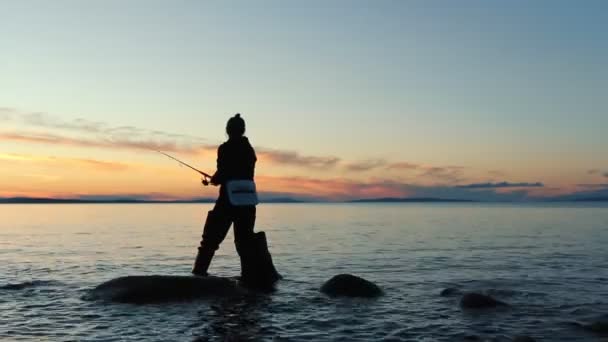 Mujer pescador captura peces con varilla giratoria en el lago al atardecer. Pesca nocturna — Vídeos de Stock