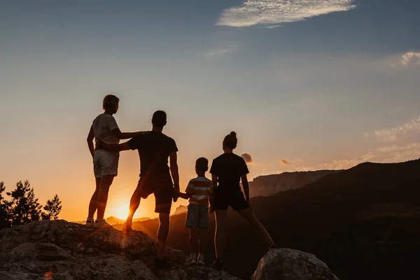 Famille accueillante embrassant avec deux enfants, un fils et une fille, debout sur le sommet de la montagne et regarder lever de soleil coloré et ciel bleu — Photo