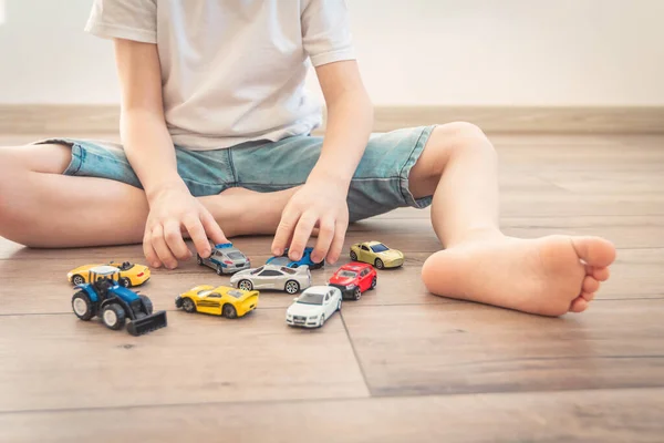 Παιδί κάθεται στο ξύλινο πάτωμα ή ζεστό παρκέ στο σπίτι και παίζει με το σύνολο των παιδικών αυτοκινήτων παιχνιδιών Royalty Free Φωτογραφίες Αρχείου