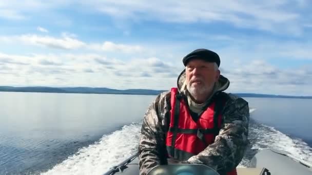 Can yeleği giymiş yaşlı gri saçlı balıkçı deniz yüzeyinde yüzen motorlu tekne kullanıyor. — Stok video