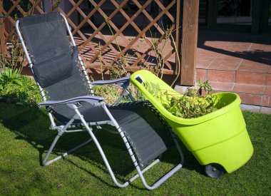 Bir iskemle ve bir evin bahçesindeki çimlerin üzerinde kesilmiş dallarla dolu bir sepet.