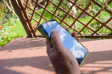 Terasta elinde bir bahçe olan akıllı bir telefonla gökyüzünün yansıması. 