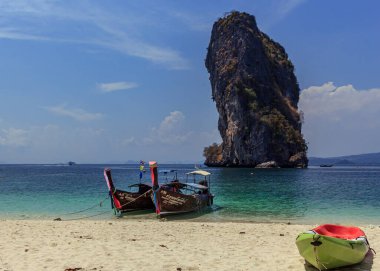 Krabi, Tayland - 29 Mart 2019: Tiran mavisi suda geleneksel ahşap kuyruk teknesi, ve beyaz kumsalda yeşil kano, ada turu, büyük kaya arka planı