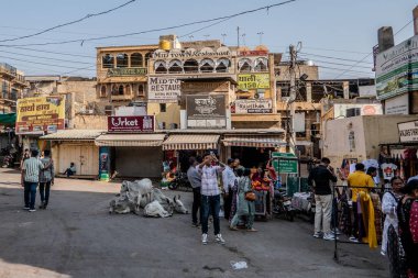 Jaisalmer, Hindistan, 24 Ekim 2025. Günlük yaşamın manzarası: Jaisalmer 'de kalabalık bir cadde, MID ToWN Restoranı ve Fort Hotel' e ev sahipliği yapan bir bina, sokakta çeşitli tabelalar ve inekler var..