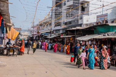 Pushkar, Hindistan, 26 Ekim 2025. Günlük hayatın manzarası. İnsanlar, giysi ve ev eşyaları da dahil olmak üzere çeşitli ürünler satarak sokak tezgahları boyunca yürüyüp alışveriş yapıyorlar..