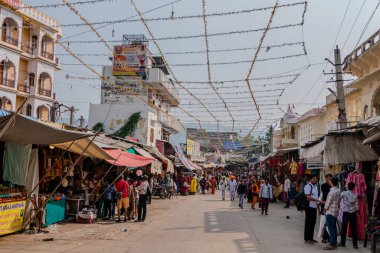 Pushkar, Hindistan, 26 Ekim 2025. Günlük hayatın manzarası. İnsanlar, giysi ve ev eşyaları da dahil olmak üzere çeşitli ürünler satarak sokak tezgahları boyunca yürüyüp alışveriş yapıyorlar..