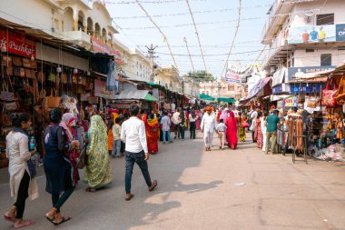 Pushkar, Hindistan, 26 Ekim 2025. Günlük hayatın manzarası. İnsanlar, giysi ve ev eşyaları da dahil olmak üzere çeşitli ürünler satarak sokak tezgahları boyunca yürüyüp alışveriş yapıyorlar..