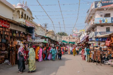 Pushkar, Hindistan, 26 Ekim 2025. Günlük hayatın manzarası. İnsanlar, giysi ve ev eşyaları da dahil olmak üzere çeşitli ürünler satarak sokak tezgahları boyunca yürüyüp alışveriş yapıyorlar..