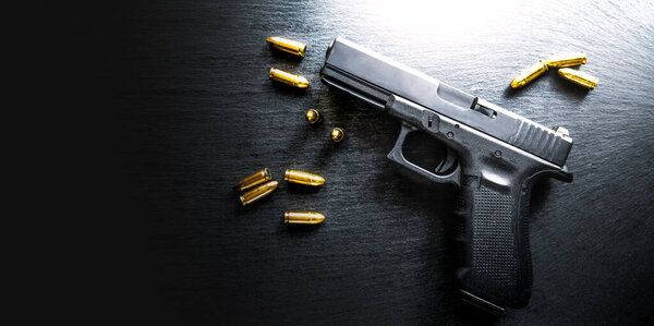 Detail on hand gun on black table banner or panorama photo on dark stone table top view. Gun shop with ammunition. 9 mm pistol gun weapon and bullets.