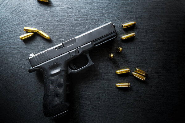 Top view of hand gun on black background with bullets around. 9mm pistol with ammunition on dark table.