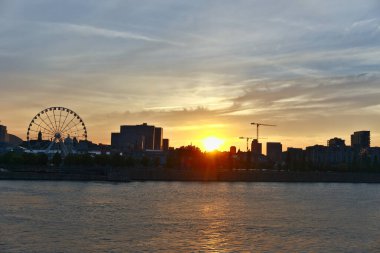 Montreal 'in ufuk çizgisi manzarası ve gün batımında Old Port' taki Grand Ferris Wheel. Saint Laurent nehrindeki güneş ışınlarının yansımaları.