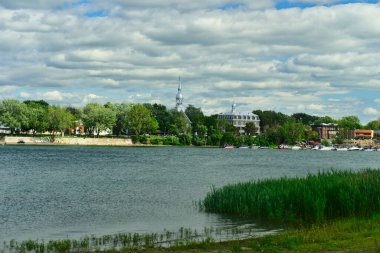 Bulutlu bir yaz gününde Montreal 'deki Saint Lawrence (Laurent) Nehri' ndeki Boucherville Ulusal Parkı 'nda Boucherville marinası. Nehir kıyısındaki ağaçlar ve çimenler.