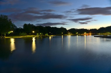 Bulutlu bir yaz gününde Beaver Gölü, Mount Royal, Montreal, QC, Kanada 'nın alacakaranlık mavi saatinde uzun bir pozlama. Işıklar ve ağaçlar gölü yansıtıyor..