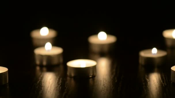 Много маленьких горящих свечей на черном столе — стоковое видео