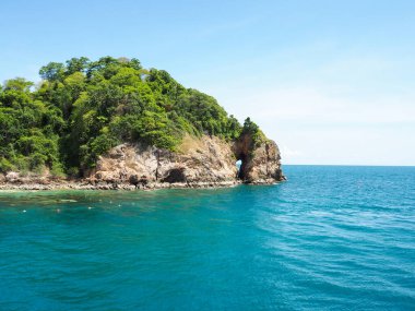 Mavi denizde beyaz gökyüzü ve bulutlarla dolu bir ada.