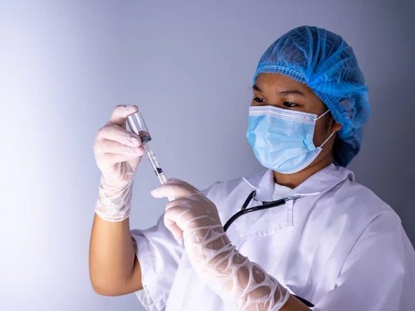 Studio portrait of a female doctor wearing a mask and wearing a hat. In hand was a bottle of vaccine and a sling of syringes. standing on a white background. Studio shot background, COVID-19 concept