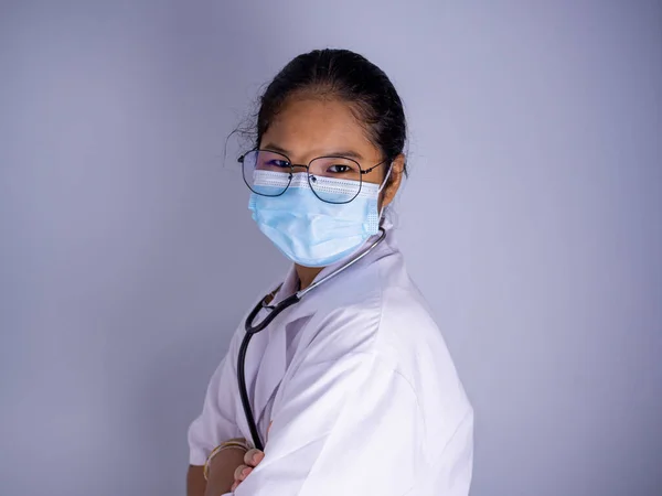 Portrait of a female doctor wearing a mask and wearing glasses standing with arms crossed on a white background