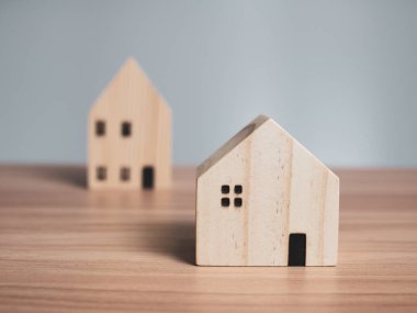 Ahşap bir masanın üzerine yerleştirilmiş iki ahşap model ev. açık gri arkaplanlı