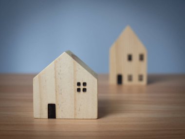 Ahşap bir masanın üzerine yerleştirilmiş iki ahşap model ev. açık gri arkaplanlı