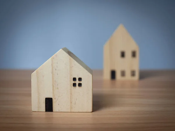 Ahşap bir masanın üzerine yerleştirilmiş iki ahşap model ev. açık gri arkaplanlı