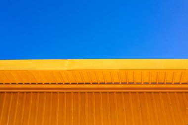 Asgari mimari tarzında mavi gökyüzü olan sarı metal bina duvarı, kentsel ve inşaat konsepti için renk kontrast ile temiz geometrik tasarım arka planı.