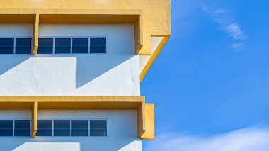 Mavi gökyüzü ve güneş ışığı gölgesi ile modern sarı ve beyaz bina cephesi, minimal mimari arka plan, geometrik şehir tasarımı ve soyut yapı kavramı.