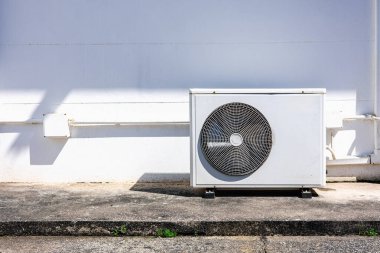 Beyaz duvarda, güneş ışığı gölgesi, enerji verimliliği ve ev soğutma teknolojisi için modern HVAC sistem kavramı olan klima kompresörü ünitesi..
