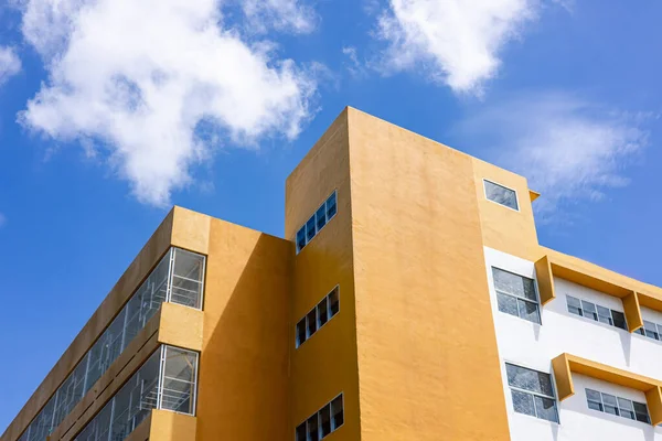 Mavi gökyüzü altında sarı ve beyaz cepheli modern minimalist bina, geometrik mimari tasarım temiz çizgiler, parlak renkler ve şehir basitliğini gösteriyor.