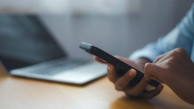 Masasında dizüstü bilgisayarı olan akıllı telefon kullanan bir iş adamı. Dijital bağlantı ve işyeri teknolojisini temsil eden modern iletişim ve mobil çalışma kavramı.