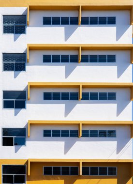 Modern beyaz ve sarı bina cephesi geometrik gölge ve minimal mimari tasarımı ile. Simetri çizgileri, pencere yapısı ve kentsel çağdaş biçime sahip soyut desen.