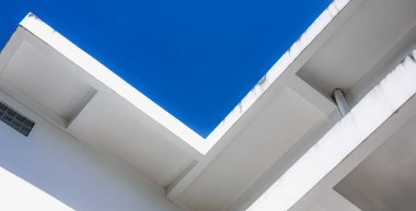 Temiz geometrik çizgiler ve parlak mavi gökyüzü ile modern beyaz binanın soyut minimal mimarisi, basitlik, yapı ve çağdaş kentsel tasarım kavramını gösterir..