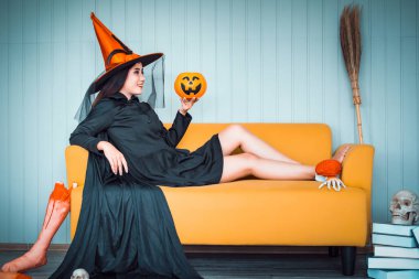 Cadı gibi giyinmiş çekici bir Asyalı kadın elinde fenerle sarı koltukta oturuyor, Cadılar Bayramı tatillerinde sinematik bir tonda.. 