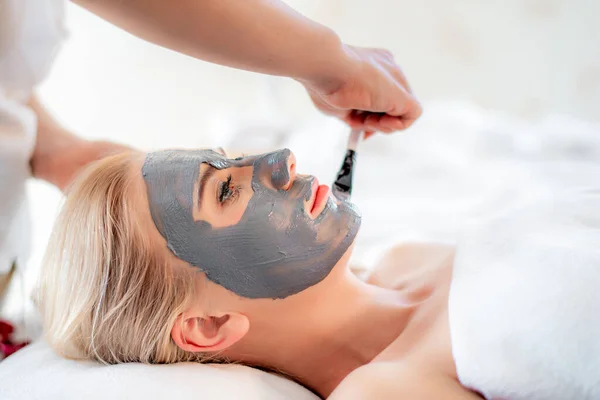 Beautiful young attractive Caucasian woman having massage and masking face with natural clay for skin care by Thai Masseur in aroma spa salon. Beauty treatment and body care concept.