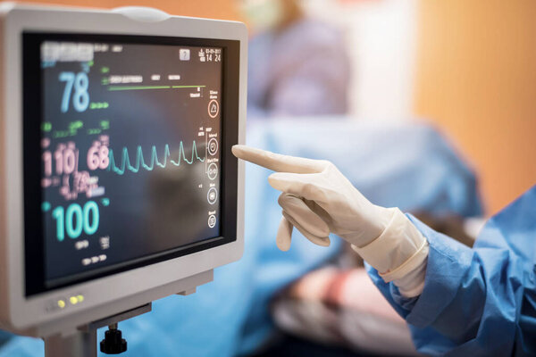 Electrocardiogram in hospital surgery operating emergency room showing patient heart rate with blur team of surgeons background 