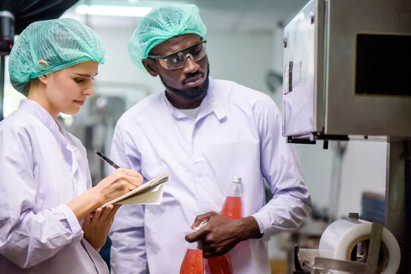 Quality control woman and man wearing a lab coat to checking juice industrial process at factory. Teamwork at production line successful concept