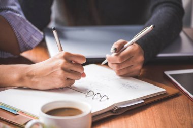 Toplantıda kalem ve veri tablosu olan iş adamlarının eli 