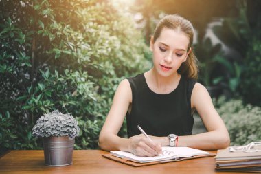 Güzel genç bayan not defterine not al, sabah bir kafein bahçesinde oturuyor..
