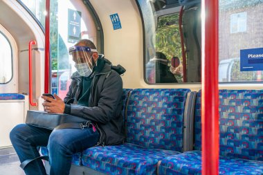 Londra, İngiltere - 23 Ekim 2020: COVID-19 salgını sırasında Londra metrosunda seyahat eden yüz maskesi takan Hintli adam - 017