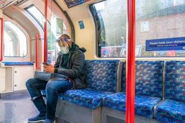 Londra, İngiltere - 23 Ekim 2020: COVID-19 salgını sırasında Londra metrosunda seyahat eden yüz maskesi takan Hintli adam - 019