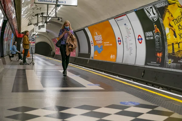 COVID-19 salgını sırasında Londra metro istasyonunda cep telefonu kullanarak yürüyen güzel sarışın kadın - 036