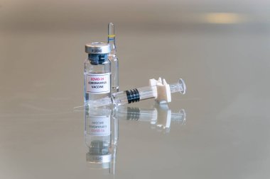Yakın plan bir COVID 19 Coronvavirus aşısı şişesi. Önünde şırınga, sağında iğne ucu var. 100.