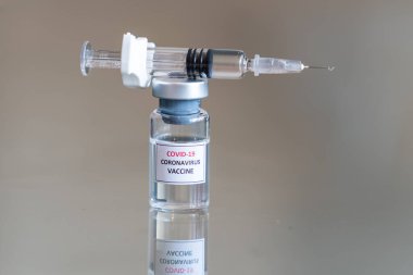 COVID-19 Coronavirus aşısı olarak etiketlenmiş tıbbi bir şişenin yakından görüntüsü. İlaç dozunu askıya alma çözeltisi. Üzerinde dolu bir şırınga ve sivri iğne var.