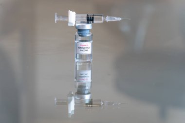 COVID-19 Coronavirus aşısı olarak etiketlenmiş bir tıbbi şişenin yakından görüntüsü. İlaç dozunu askıya alma çözeltisi. Üzerinde dolu bir şırınga ve keskin bir iğne var.