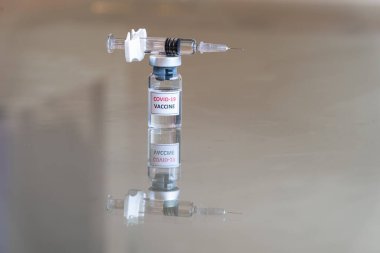 COVID-19 Coronavirus aşısı olarak etiketlenmiş tıbbi bir şişenin görüntüsü. İlaç dozajı süspansiyon çözeltisi ile dolu bir şırınga ve sivri iğne ucunda bir damla ile dengelenmiş - 013