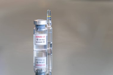 COVID-19 Coronavirus olarak etiketlenmiş tıbbi şişenin yakından görüntüsü. Virüs biyolojik tehlike aşısı. Arka tarafta ampul ile askıya alındı.
